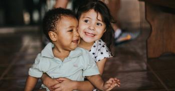 Photograph of a young girl hugging a baby boy