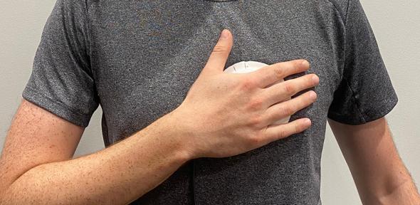 Person wearing a grey t-shirt holding a palm-sized device to their chest