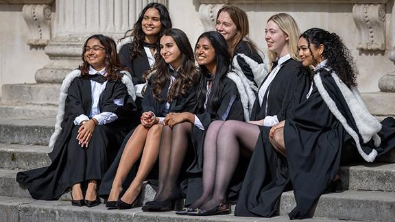 Seven female graduands in formal wear and graduation robes.